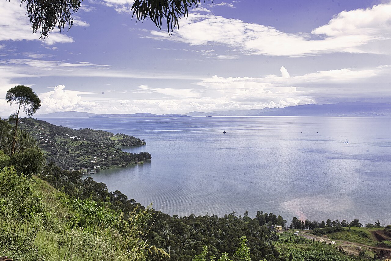 Elevated view over Lake Kivu with a green wooded shoreline curving into the bay under a bright sky